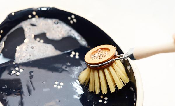 Ein blauer Teller mit weißen Blumenmustern und Rändern wird mit der Spielbürste gereinigt und dabei schräg gehalten. Stärkerer Fokus aufs Geschehen.
